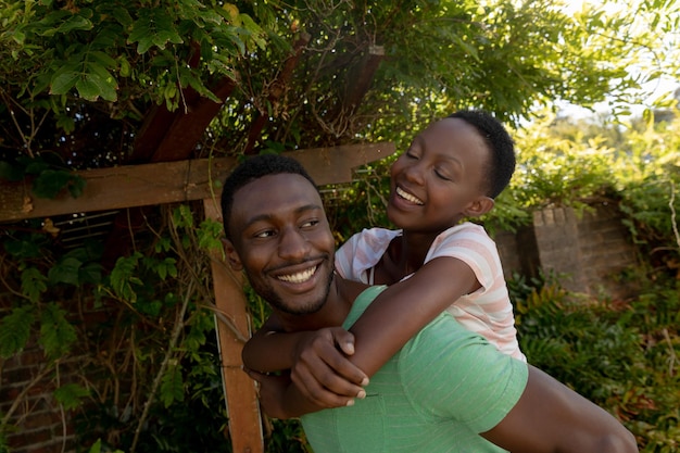Afroamerykanie para na słonecznym tarasie ogrodowym mężczyzna niosący ją uśmiechając się. przebywanie w domu w izolacji podczas blokady kwarantanny.