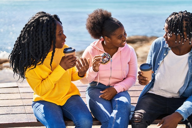 Afroamerykanie przyjaciele jedzą śniadanie siedząc na ławce nad morzem