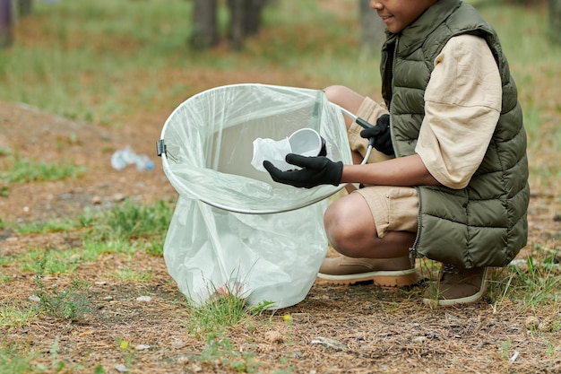 Zdjęcie afroamerykanin chłopiec wkłada śmieci do torby na zewnątrz