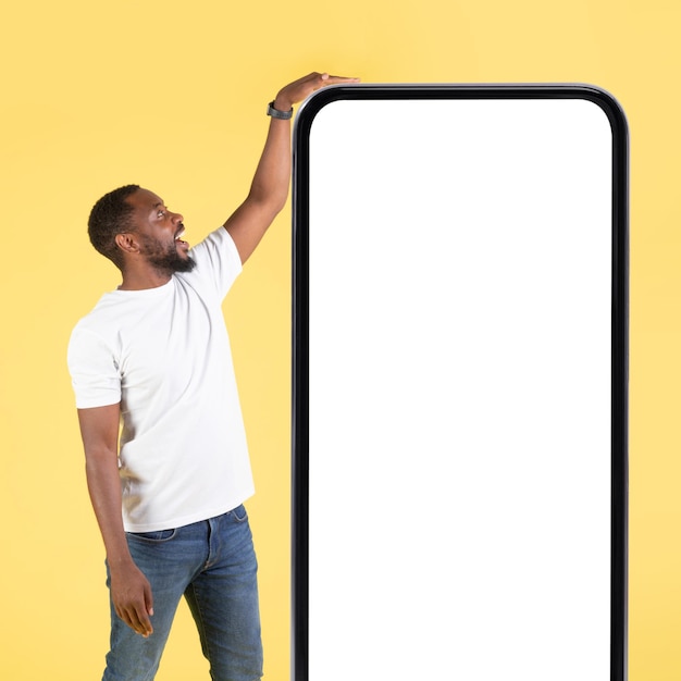 Afroamerykanin dotyka dużego telefonu stojącego na żółtym tle