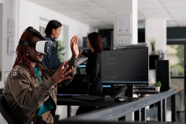 Afroamerykanin inżynier systemowy w goglach rzeczywistości wirtualnej pracujący nad rozwojem programu bezpieczeństwa w biurze big data, programista z zestawem słuchawkowym vr kodujący skrypt html z bazą danych.
