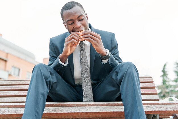 Afroamerykanin je burgera w parku na świeżym powietrzu podczas korzystania ze swojego smartfona