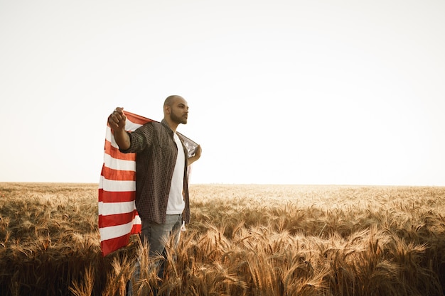 Afroamerykanin młody człowiek trzymający flagę narodową usa przez pole pszenicy