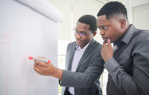 Afroamerykanin młody mężczyzna piszący notatkę na przezroczystej tablicy do wycierania i myślący o rozwiązaniu dla niego problemów związanych z pracą, koledzy mający spotkanie biznesowe