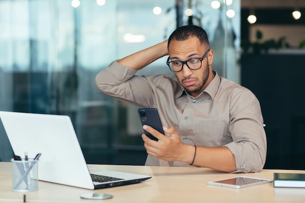 Afroamerykanin patrzący i myślący przez telefon biznesmen pracujący z laptopem i komputerem