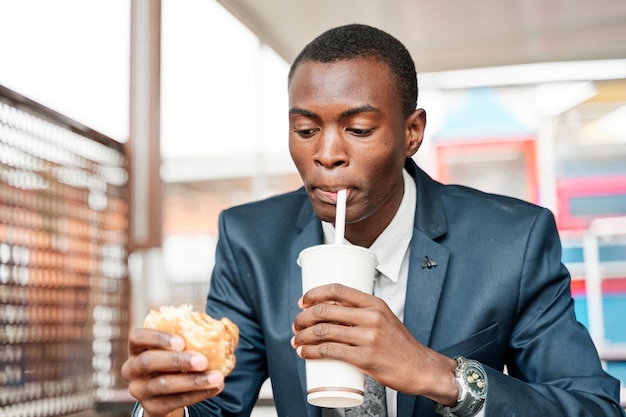 Afroamerykanin pijący napój gazowany z hamburgerem w ręku