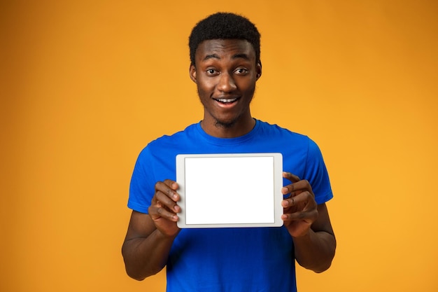 Afroamerykanin pokazuje pusty cyfrowy ekran tabletu z miejscem na kopię w żółtym studiu