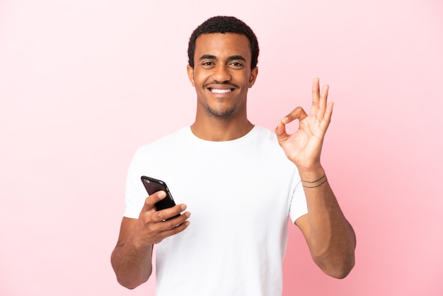 Afroamerykanin Przystojny Mężczyzna Na Na Białym Tle Różowym Tle Za Pomocą Telefonu Komórkowego I Robi Znak Ok