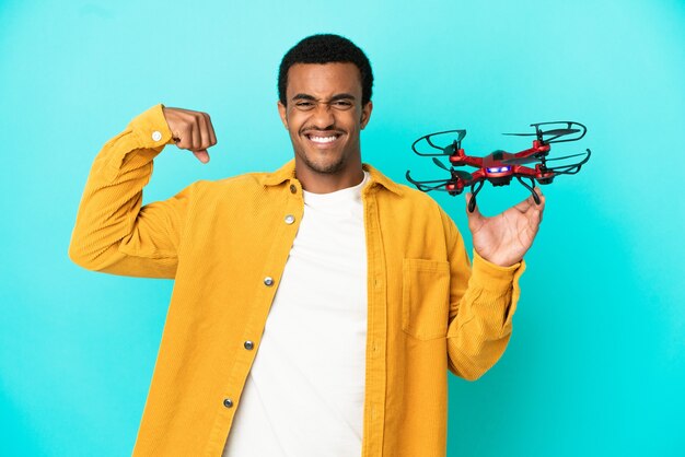 Afroamerykanin, przystojny mężczyzna, trzymający drona na odosobnionym niebieskim tle, wykonujący silny gest