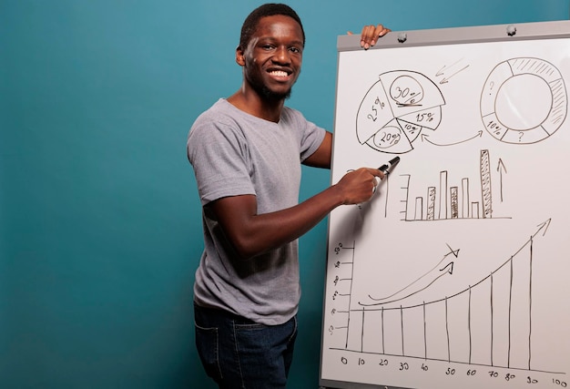 Afroamerykanin robi prezentację projektu z wykresami i statystykami finansowymi na tablicy na niebieskim tle. Konsultant menedżera wykorzystujący afisz biznesowy do reklamy.