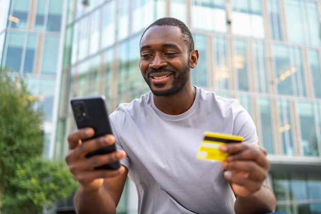 Afroamerykanin robi zakupy online trzymając smartfon płacąc złotą kartą kredytową facet na Urban