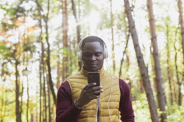 Afroamerykanin słucha muzyki w jesiennym parku Gadget app i koncepcja usługi przesyłania strumieniowego