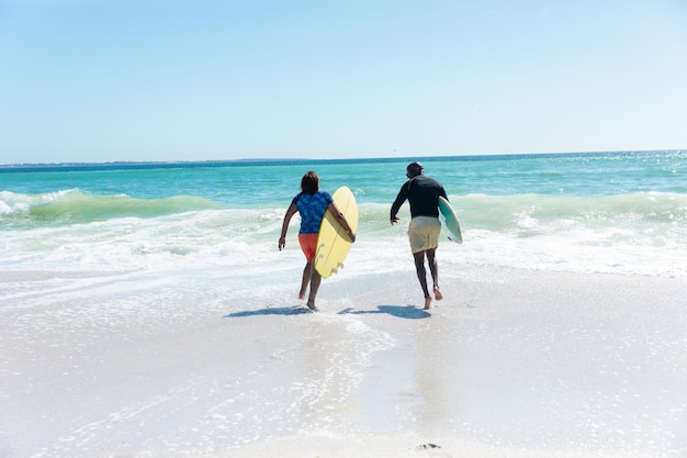 Afroamerykanin starszy para niosąca deski surfingowe biegnące w kierunku fal na plaży z miejsca na kopię