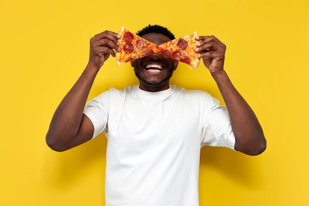 Afroamerykanin w białej koszulce trzyma dwa kawałki pizzy przed oczami i krzyczy