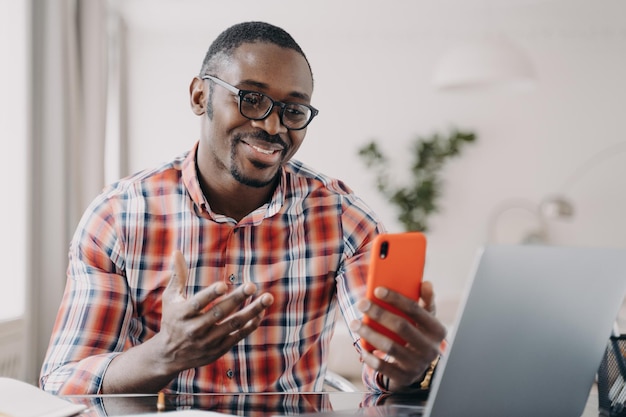 Afroamerykanin w okularach rozmawia online przez połączenie wideo, trzymając smartfon za pomocą aplikacji mobilnych