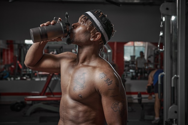 Afroamerykanin wysportowany mężczyzna z nagim torsem do picia wody lub odżywiania sportowego ze szkła po