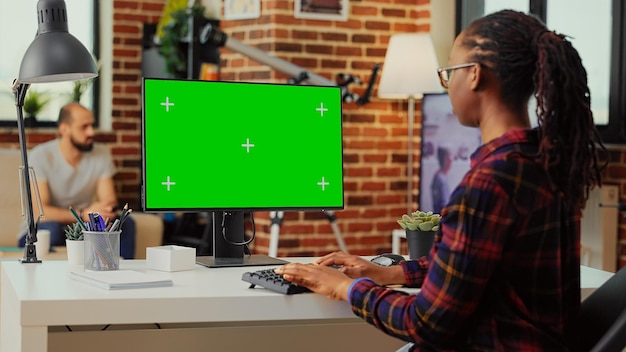 Afroamerykanin za pomocą monitora, aby sprawdzić szablon greenscreen na na białym tle, patrząc na tło klucza chroma z makieta. Praca z copyspace na ekranie komputera.