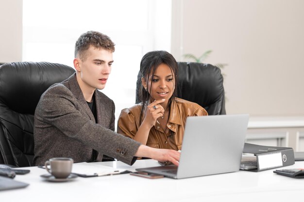 Afroamerykanka bizneswoman w biurze z młodym kolegą pracującym na laptopie