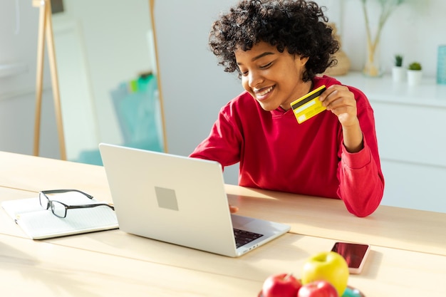 Afroamerykanka korzystająca z laptopa, robiąca zakupy online, płacąca złotą kartą kredytową, dziewczyna siedząca w domu