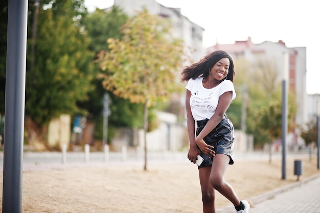 Afroamerykanka o ciemnej karnacji, szczupła modelka pozowana w czarnych skórzanych szortach i białej koszulce