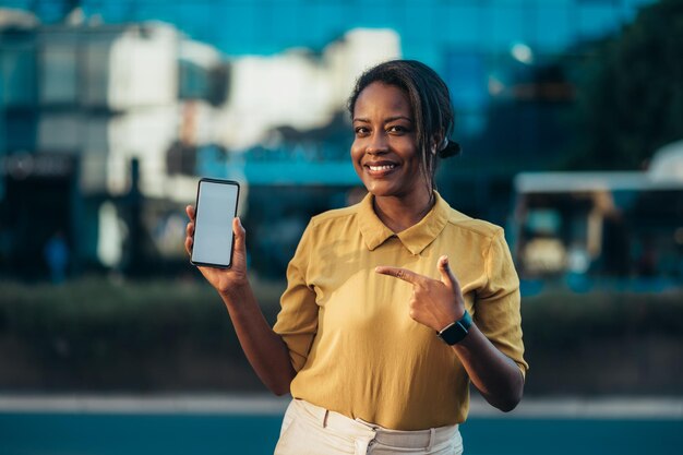 Afroamerykanka pokazuje smartfon stojąc na ulicy miasta