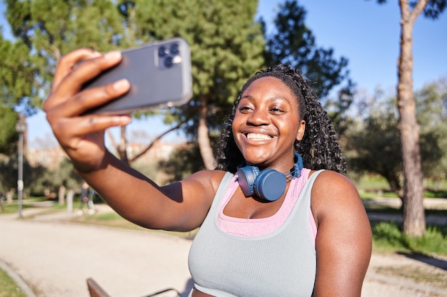 Afroamerykanka robiąca selfie przed treningiem, kręcona kobieta w odzieży sportowej.