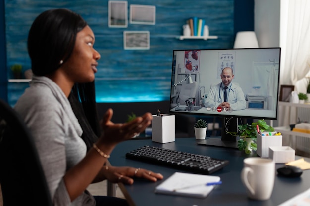 Afroamerykanka rozmawia z lekarzem podczas wideorozmowy, aby otrzymać poradę medyczną na temat telemedycyny i telezdrowia w domu. Młody pacjent korzystający ze zdalnej konferencji online, aby porozmawiać z lekarzem