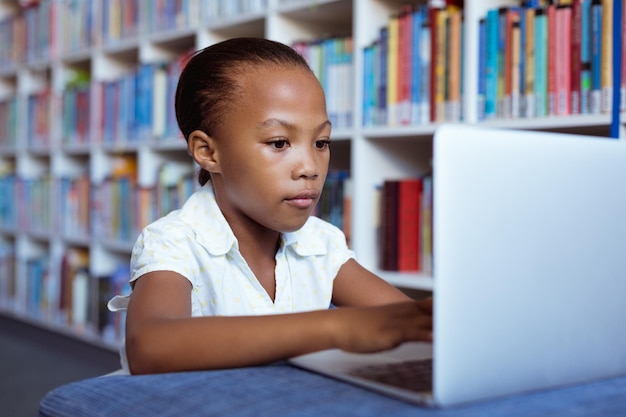 Afroamerykanka uczennica przy biurku w bibliotece szkolnej, koncentrując się za pomocą laptopa