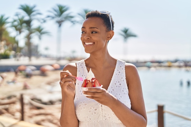 Afroamerykanka uśmiecha się pewnie, jedząc lody nad morzem