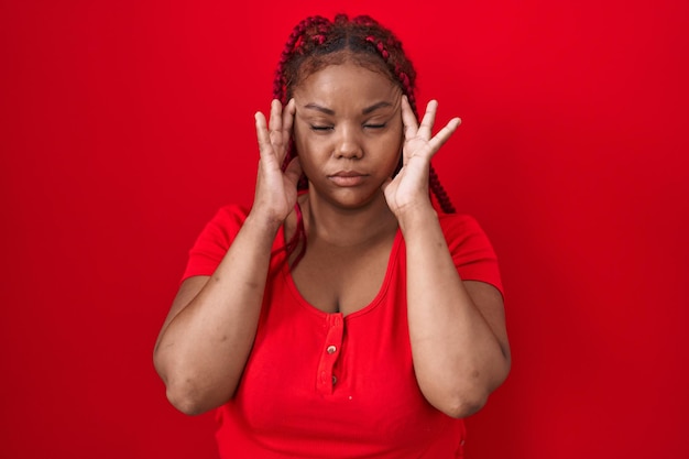 Afroamerykanka z plecionymi włosami stojąca na czerwonym tle z ręką na głowie z powodu bólu głowy z powodu stresu cierpiącego na migrenę