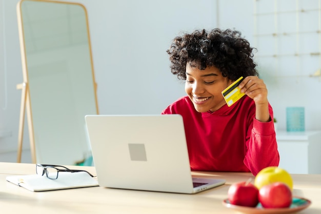 Afroamerykanka za pomocą laptopa robi zakupy online płacąc złotą kartą kredytową Dziewczyna siedzi w domu kupując przez Internet wprowadź dane karty kredytowej Zakupy online Usługa dostawy e-commerce