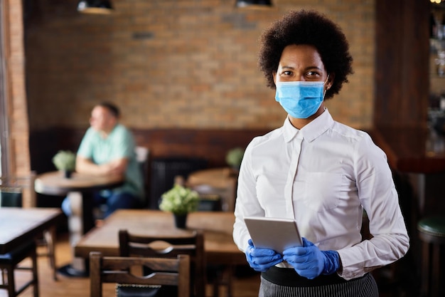 Afroamerykańska kelnerka nosząca maskę ochronną i rękawiczki podczas pracy w kawiarni