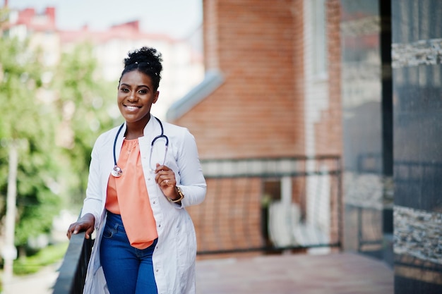 Afroamerykańska lekarka w fartuchu laboratoryjnym ze stetoskopem postawiona na zewnątrz przed kliniką