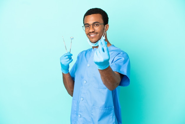 Afroamerykański dentysta trzymający narzędzia na odosobnionym niebieskim tle gestu zarabiania pieniędzy