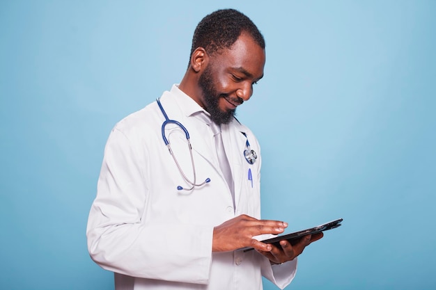 Afroamerykański lekarz ogólny przeglądający internet na swoim tabletie w poszukiwaniu informacji medycznych Czarny lekarz z stetoskopem używający cyfrowego urządzenia do badań zdrowotnych