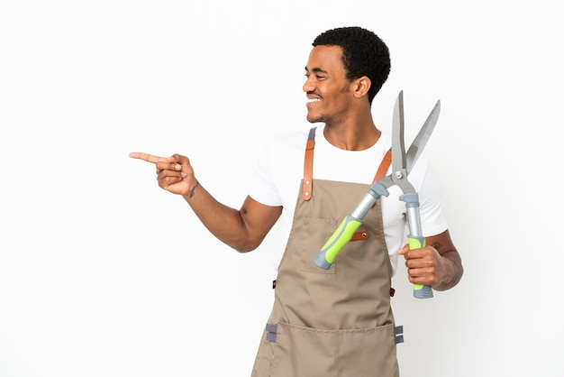 Afroamerykański ogrodnik mężczyzna trzymający nożyce do przycinania na białym tle, wskazujący palec w bok i prezentujący produkt