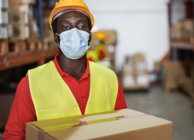 Afroamerykański pracownik magazynu trzymający pakiet podczas noszenia maski ochronnej na koronawirusa