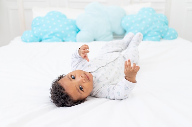 Afroamerykańskie małe dziecko na białym łóżku w sypialni leży w piżamie