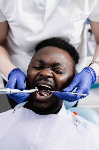 Afrykanin boi się dentysty Dentysta konsultuje się i wierci zęby przestraszonego mężczyzny w stomatologii Leczenie zębów i bólu zęba w stomatologii