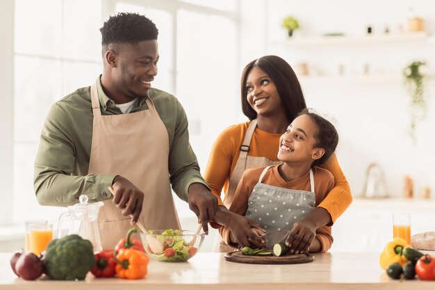 Afrykańscy rodzice i córka wspólnie gotują sałatkę w kuchni