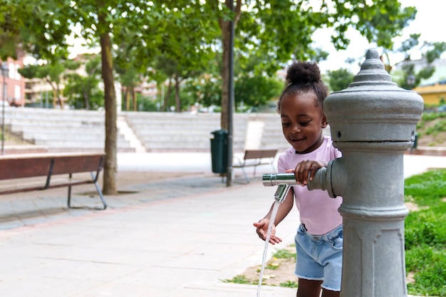 Afrykańska dziewczyna bawiąca się w kolorowym parku miejskim Fontanna wodna szczęśliwie rozpryskująca