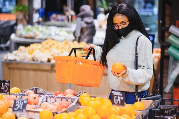 Afrykańska kobieta nosi jednorazową maskę medyczną. Zakupy w supermarkecie podczas wybuchu pandemii koronawirusa. Czas epidemii.