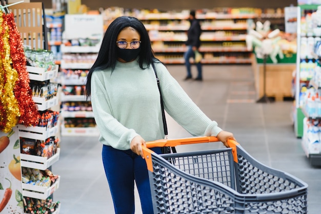 Afrykańska kobieta nosi jednorazową maskę medyczną. Zakupy w supermarkecie podczas wybuchu pandemii koronawirusa. Czas epidemii.