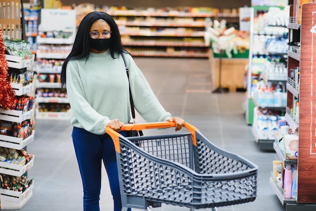 Afrykańska kobieta nosząca jednorazową maskę medyczną robiącą zakupy w supermarkecie podczas wybuchu pandemii koronawirusa Czas epidemii