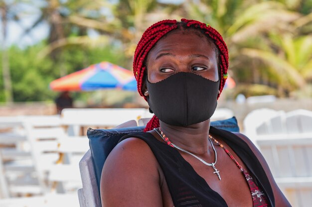 Zdjęcie afrykańska kobieta siedząca na plaży z czarną maską do ust w labadi accra ghana afryka zachodnia