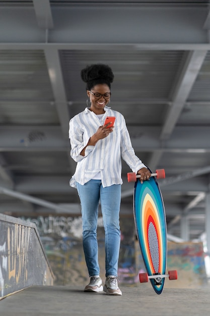 Afrykańska łyżwiarka z longboardem trzyma powiadomienie o odczytywaniu sieci w przestrzeni dla deskorolkarzy