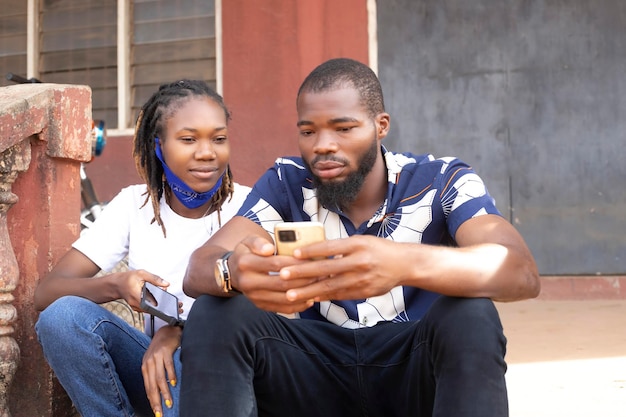 Afrykańska para za pomocą gadżetów ładna dziewczyna z Afro wpisuje wiadomość na telefonie komórkowym, podczas gdy jej chłopak siedzi obok niej, patrząc w dół na ekran jej smartfona