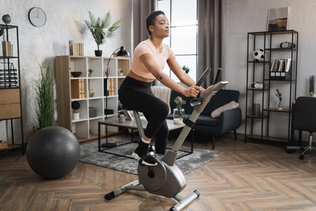 Afrykańska Uśmiechnięta Młoda Sportsmenka Robi Cardio Na Rowerze Stacjonarnym