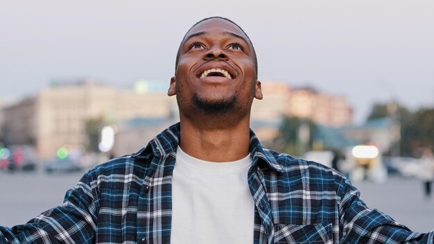 Afrykański Amerykanin szczęśliwy młody facet w zwykłej koszulce odizolowany na ulicy miasta na zewnątrz patrząc na kamerę