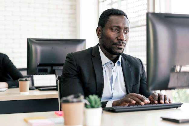 Afrykański biznesmen pisze na klawiaturze i z zamiarem patrzy na ekran w miejscu pracy przy biurku z miejscem na kopię